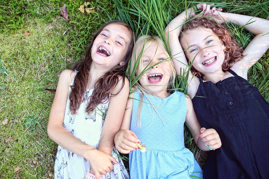 3 Kinder liegen freudestrahlen auf der Wiese